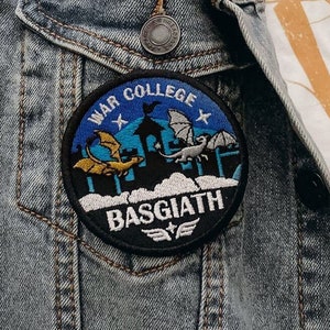 May include: A blue and black embroidered patch with the text "War College" and "Basgiath" on a denim jacket.