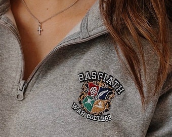 May include: Grey sweatshirt with a zip and a small embroidered crest that says "Basquiath War College".