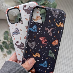 May include: Two phone cases featuring dragon patterns. One is white with brown, grey, and orange dragons, and lightning bolts. The other is black with colourful dragons and stars.
