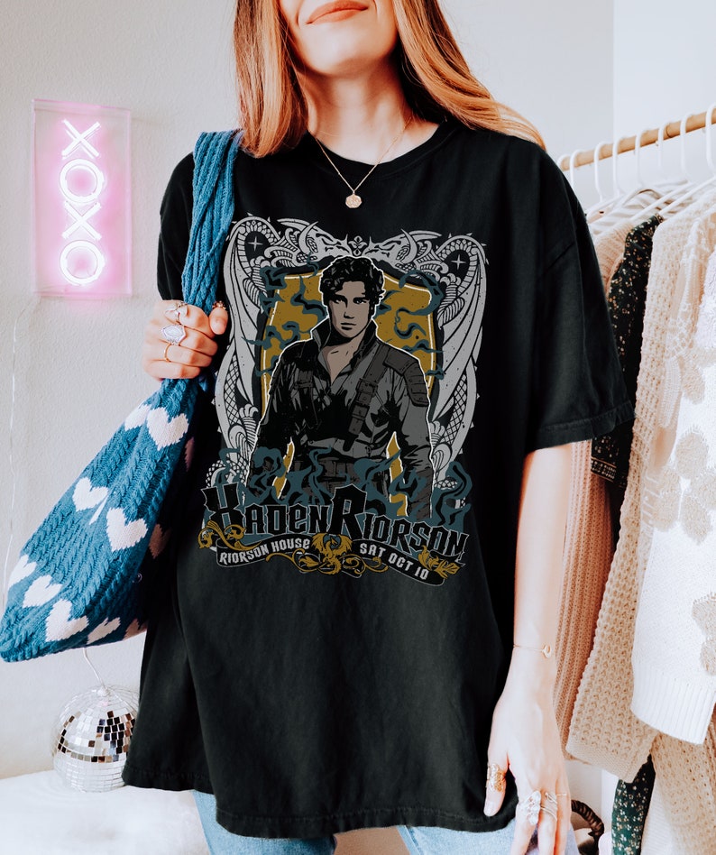 May include: Black t-shirt featuring a graphic print of a man with a sword and a dragon design. The text on the shirt reads "Haden Rierson, Rierson House, Sat Oct 10".