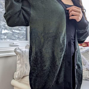 May include: A dark green and black cardigan with a button-up front. The cardigan has a subtle ombre effect, fading from dark green to black.