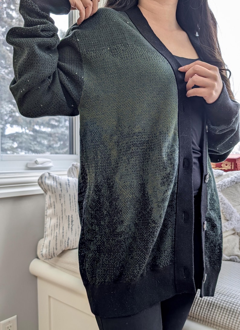 May include: A dark green and black cardigan with a button-up front. The cardigan has a subtle ombre effect, fading from dark green to black.