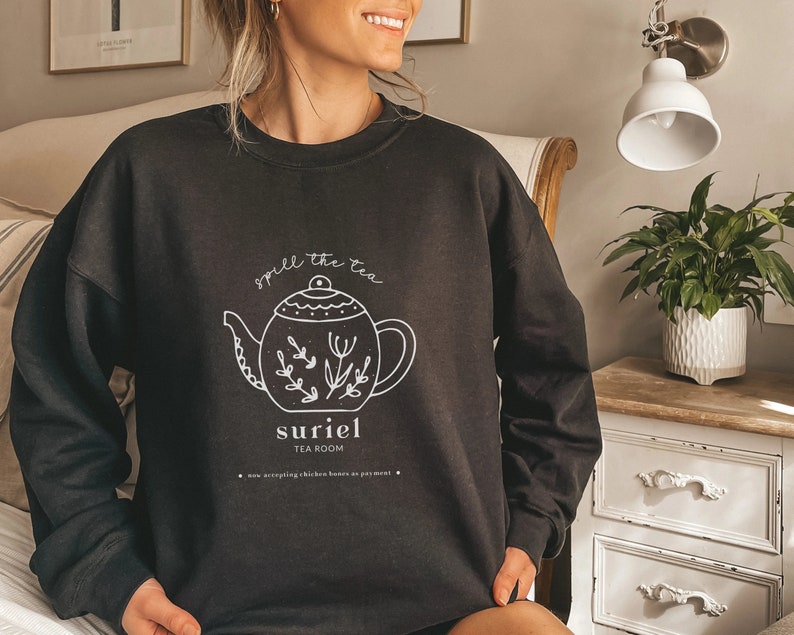 May include: Black sweatshirt with a white graphic of a teapot and the text "spill the tea suriel tea room now accepting chicken bones as payment".