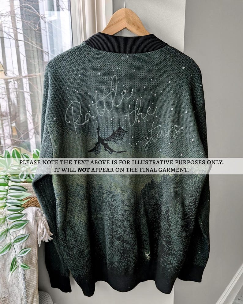 May include: A dark green long-sleeved sweater with a black collar and a white design of a dragon flying through a starry sky. The text "Rattle the stars" is written in white above the dragon.