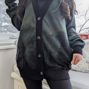 May include: A dark green and black cardigan with a button-up front and a subtle pattern. The cardigan has a V-neck and long sleeves.