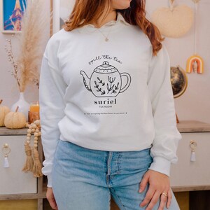 May include: White sweatshirt with a black and white illustration of a teapot with the text "spill the tea" and "suriel tea room".