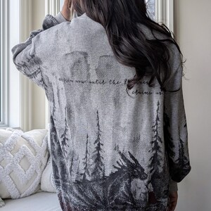 May include: Gray sweater with a forest and dragon design. The back of the sweater features a detailed illustration of a dragon, trees, and the text "Now now until the darkness claims us." The sweater is a comfortable, casual style.
