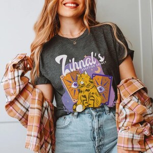 May include: A dark gray t-shirt with the text "Zihnal's Adoption Agency" and a cartoon illustration of a cat with a purple, blue, and yellow background.