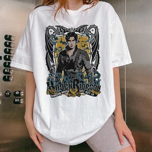 May include: White t-shirt featuring a graphic print of a man with a dragon design. The text on the shirt reads "Riderson House Sat Oct 10".