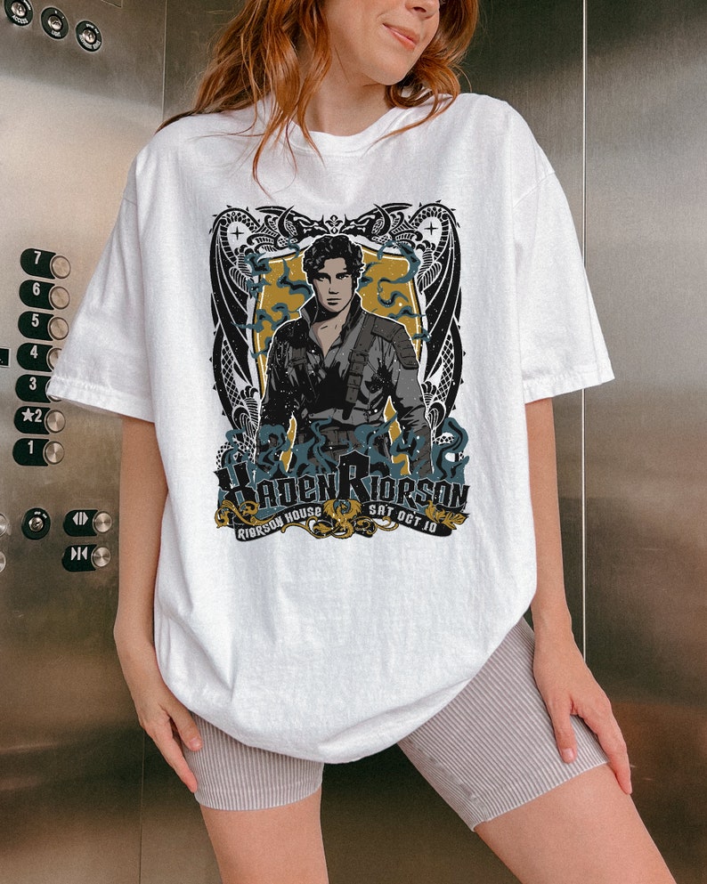 May include: White t-shirt featuring a graphic print of a man with a dragon design. The text on the shirt reads "Riderson House Sat Oct 10".