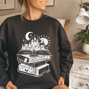 May include: Black sweatshirt with a white graphic of a castle, moon, sun, and a stack of books with the text "I have lived a thousand lives".