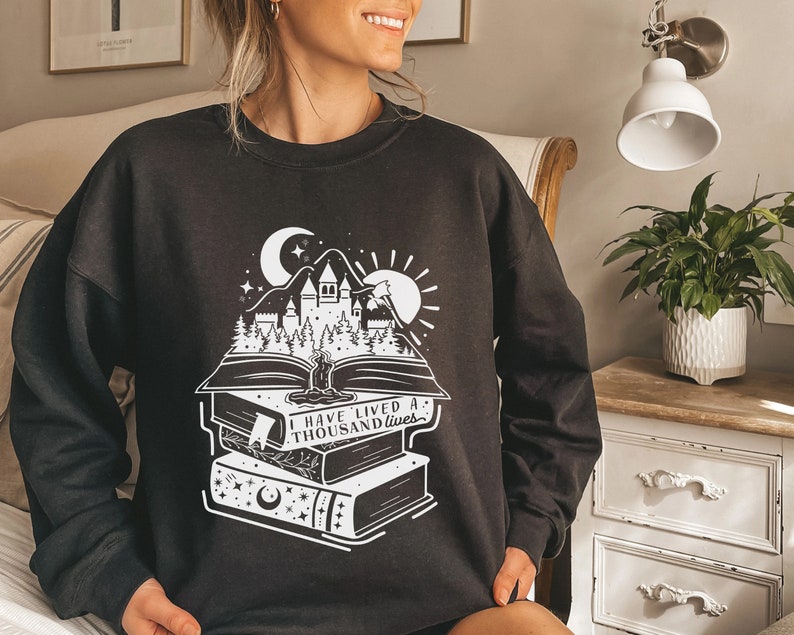 May include: Black sweatshirt with a white graphic of a castle, moon, sun, and a stack of books with the text "I have lived a thousand lives".