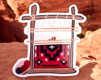 May include: A sticker of a red, black, and white patterned rug being woven on a wooden loom. The loom is made of two vertical posts connected by horizontal beams. There are balls of yarn in a basket below the loom.