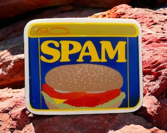 May include: A blue and yellow sticker with the word "SPAM" in yellow letters and a cartoon image of a hamburger with a tomato, lettuce, and cheese.