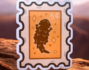 May include: A brown and white sticker with a cartoon image of a lizard on a postage stamp. The stamp has a light orange background with white stars and the text "5¢".