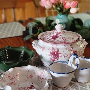 May include: A set of white ceramic bowls with pink and white marbling. The bowls have a scalloped edge and are perfect for serving a variety of dishes. The bowls are displayed on a table with a white and gray patterned tablecloth.