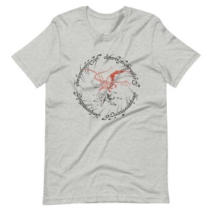 May include: A grey t-shirt with a red dragon flying over a mountain. The dragon is surrounded by a circle of text in a black font that reads "One Ring to rule them all, One Ring to find them, One Ring to bring them all, and in the darkness bind them."