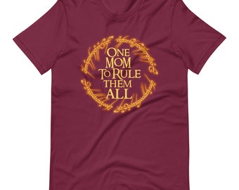 May include: Burgundy t-shirt with the text "ONE MOM TO RULE THEM ALL" in a gold, circular design. The design is reminiscent of a ring with stylized lettering. The shirt is made of a soft material.