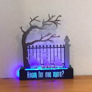 May include: A black and gray 3D printed Halloween decoration with a spooky tree, a gate, and ghosts. The base of the decoration has a blue light and the text "Room for one more?"