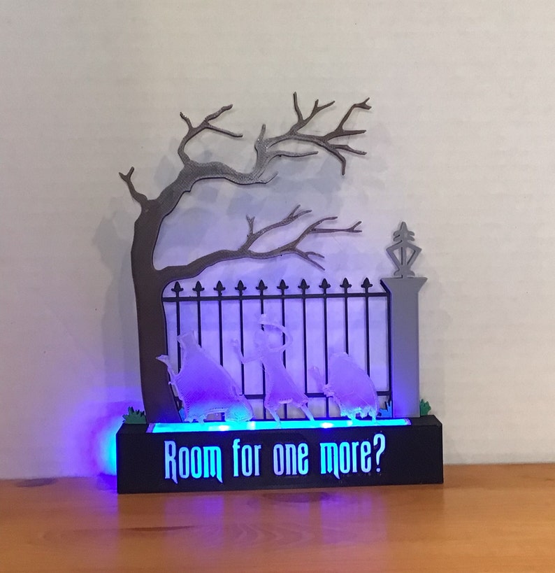 May include: A black and gray 3D printed Halloween decoration with a spooky tree, a gate, and ghosts. The base of the decoration has a blue light and the text "Room for one more?"