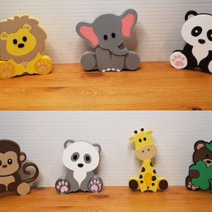 Könnte beinhalten: Satz von zehn Holztierfiguren, darunter ein Löwe, ein Elefant, ein Panda, ein Affe, eine Giraffe und ein Bär. Die Figuren sind in leuchtenden Farben bemalt und haben einen skurrilen, cartoonartigen Stil.
