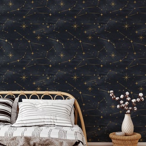 Pu&ograve; includere: Una carta da parati blu navy con un motivo a costellazione dorata. La carta da parati &egrave; mostrata in una camera da letto con un letto, cuscini e un comodino.