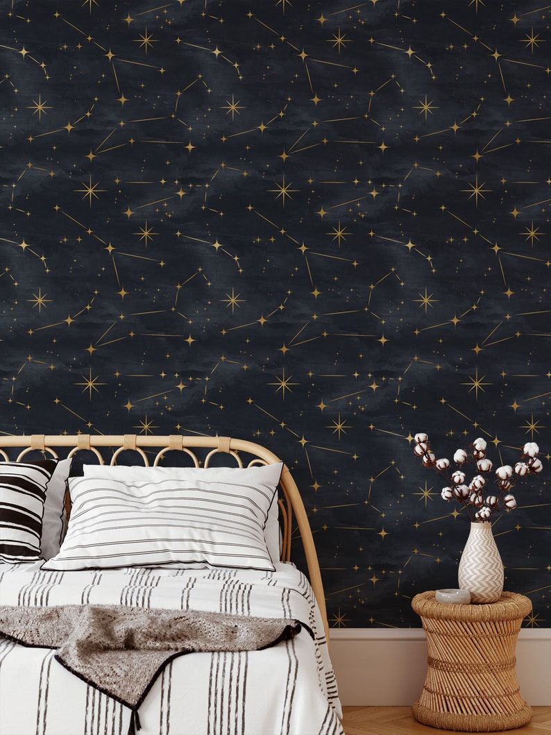 Pu&ograve; includere: Una carta da parati blu navy con un motivo a costellazione dorata. La carta da parati &egrave; mostrata in una camera da letto con un letto, cuscini e un comodino.