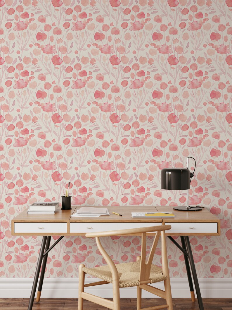 May include: A light wood desk with two drawers and a black metal frame. A chair with a woven seat and a black lamp are in front of the desk. The wall behind the desk is covered in pink floral wallpaper.