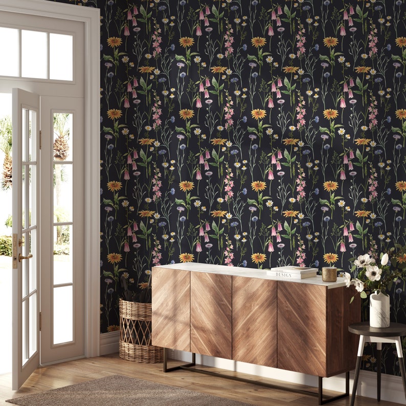 May include: A dark gray wallpaper with a floral pattern featuring pink, yellow, and white flowers. The wallpaper is displayed on a wall in a room with a wooden cabinet and a wicker basket.