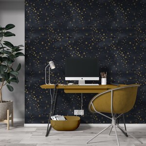 K&ouml;nnte beinhalten: Ein Homeoffice-Arbeitsplatz mit einem schwarzen Schreibtisch und einem goldenen Stuhl. Die Wand ist mit einer dunkelblauen Tapete mit einem goldenen Sternenmuster bedeckt. Ein Computermonitor, eine Lampe und ein kleiner Korb stehen auf dem Schreibtisch.