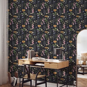 May include: A black and white floral wallpaper with a repeating pattern of pink, yellow, and blue flowers. A wooden desk with a chair and a lamp is in front of the wallpaper.