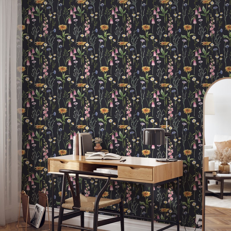 May include: A black and white floral wallpaper with a repeating pattern of pink, yellow, and blue flowers. A wooden desk with a chair and a lamp is in front of the wallpaper.
