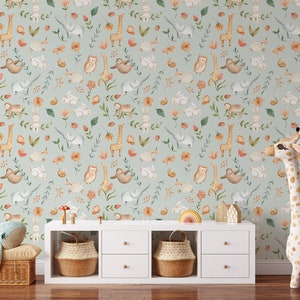 K&ouml;nnte beinhalten: Eine hellblaue Tapete mit einem sich wiederholenden Muster aus Tieren und Blumen. Zu den Tieren geh&ouml;ren Giraffen, Eulen, Faultiere, Elefanten und Kaninchen. Die Blumen sind orange, rosa und gelb. Die Tapete ist in einem Raum mit einem wei&szlig;en Regal und einem Stofftier-Giraffe zu sehen.