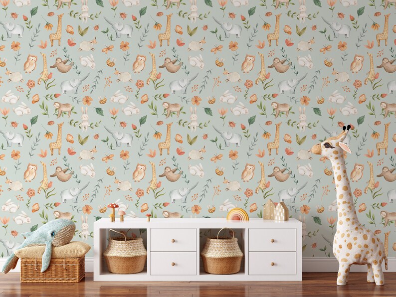 K&ouml;nnte beinhalten: Eine hellblaue Tapete mit einem sich wiederholenden Muster aus Tieren und Blumen. Zu den Tieren geh&ouml;ren Giraffen, Eulen, Faultiere, Elefanten und Kaninchen. Die Blumen sind orange, rosa und gelb. Die Tapete ist in einem Raum mit einem wei&szlig;en Regal und einem Stofftier-Giraffe zu sehen.