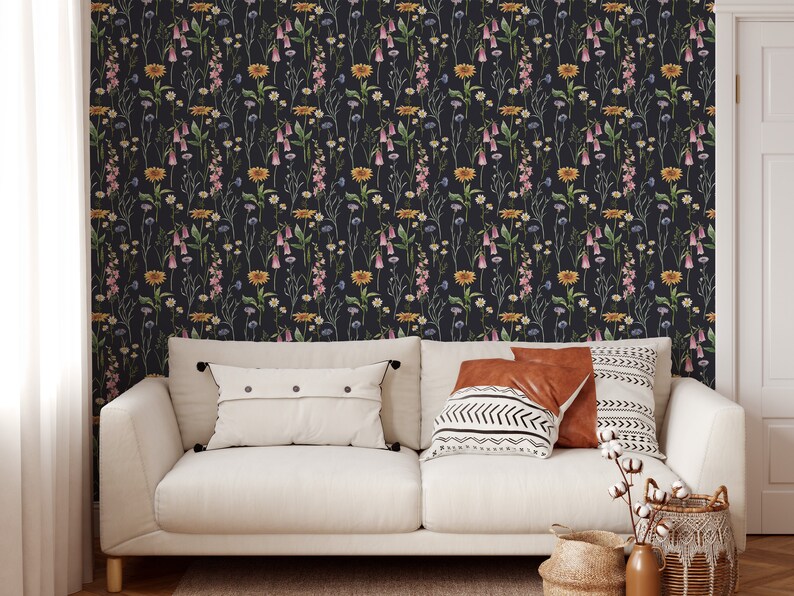 May include: A white couch with two throw pillows and a patterned throw blanket sits in front of a wall covered in a dark floral wallpaper. The wallpaper features a repeating pattern of pink, yellow, and blue flowers on a dark background.