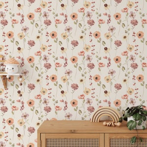 May include: A beige wallpaper with a repeating pattern of watercolour flowers in shades of pink, orange, and yellow. The flowers are arranged in a vertical pattern and are surrounded by green leaves. The wallpaper is shown in a room with a wooden dresser and a rainbow-coloured wooden toy.
