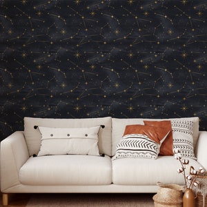 Pu&ograve; includere: Un divano bianco con due cuscini e una coperta davanti a un muro blu scuro con costellazioni dorate.