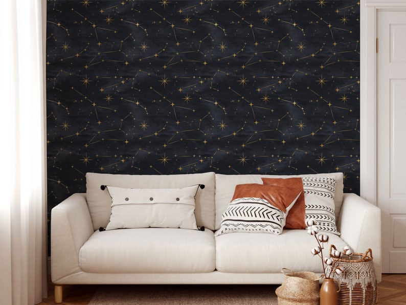 Pu&ograve; includere: Un divano bianco con due cuscini e una coperta davanti a un muro blu scuro con costellazioni dorate.