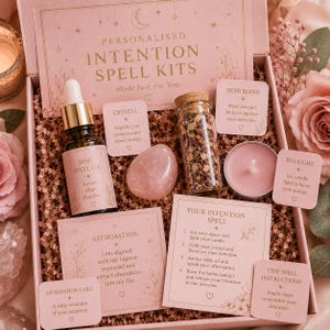 May include: A pink personalized intention spell kit with a variety of items. The kit includes a bottle of spell oil, a rose quartz crystal, a jar of herbs, a tea light candle, and affirmation cards. The box is filled with crinkle paper.