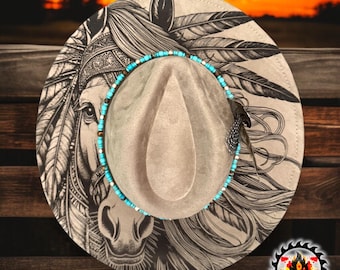 May include: A tan fedora hat with a detailed black and white horse and feather design on the brim. The hat features a turquoise and silver beaded band around the crown and a single feather. The hat is a western-themed accessory.