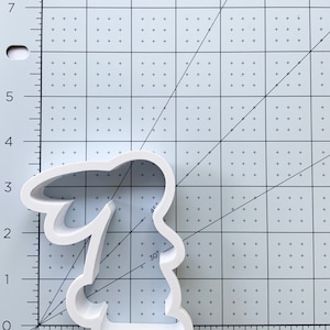 May include: White plastic cookie cutter shaped like a bunny rabbit. The cutter is approximately 3 inches tall and 2 inches wide.