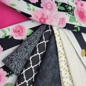 Op de afbeelding: Een verzameling stofstalen in verschillende patronen en kleuren, waaronder zwart-witte strepen, bloemenprints en een effen zwarte stof.