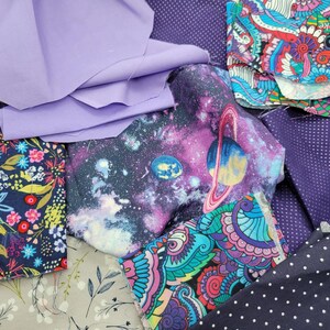 Op de afbeelding: Een verzameling stofresten in verschillende kleuren en patronen, waaronder paars, blauw, roze en wit. De stoffen hebben bloemen-, galaxy- en paisley-ontwerpen.