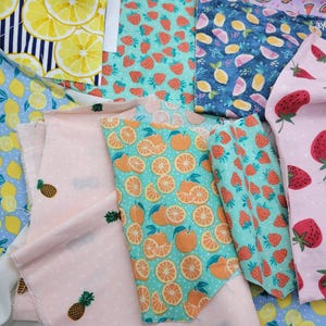 Op de afbeelding: Assortiment van stoffenresten met verschillende fruitprints. De stoffen tonen citroenen, sinaasappels, aardbeien en ananas op verschillende achtergronden, waaronder blauw, roze en groen.