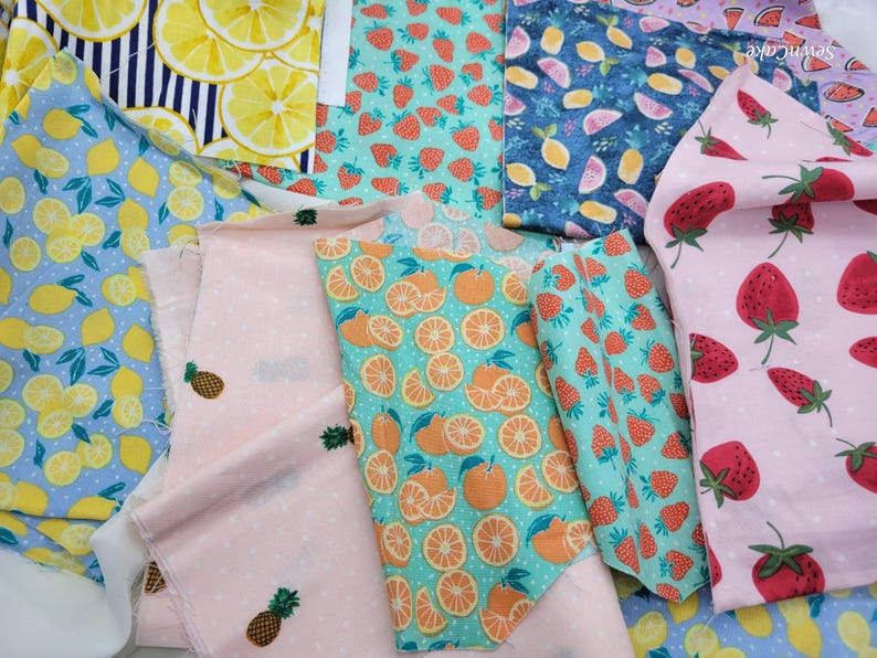 Op de afbeelding: Assortiment van stoffenresten met verschillende fruitprints. De stoffen tonen citroenen, sinaasappels, aardbeien en ananas op verschillende achtergronden, waaronder blauw, roze en groen.