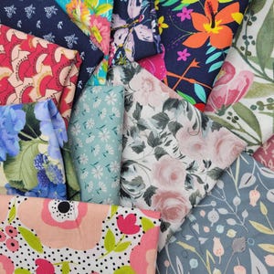 Op de afbeelding: Een verzameling stofresten met verschillende bloemenpatronen in tinten roze, blauw, groen en rood. De stoffen zijn in een stapel gelegd, waardoor de verschillende ontwerpen worden getoond.