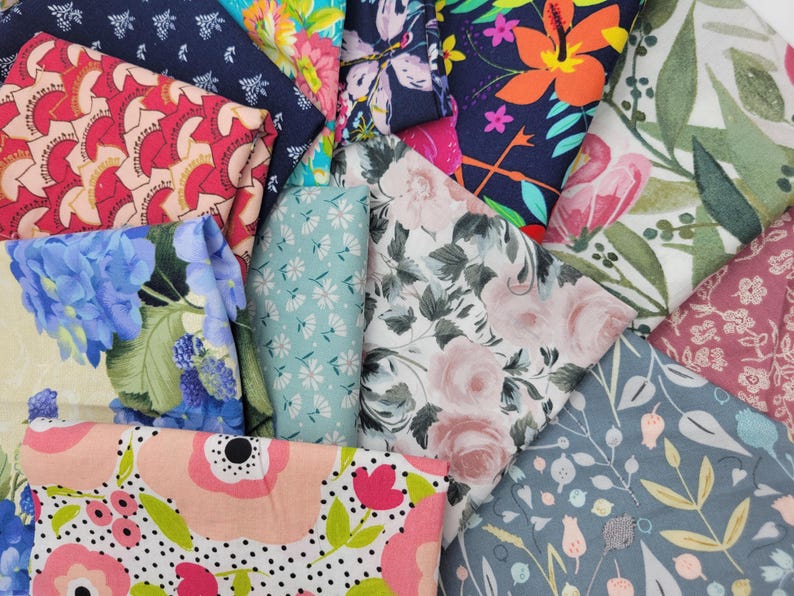 Op de afbeelding: Een verzameling stofresten met verschillende bloemenpatronen in tinten roze, blauw, groen en rood. De stoffen zijn in een stapel gelegd, waardoor de verschillende ontwerpen worden getoond.