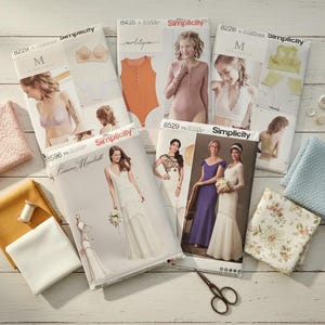 May include: A collection of Simplicity sewing patterns for lingerie and dresses, with fabric swatches, thread, and scissors. The patterns feature images of women in various garments. Additional items include buttons and lace.