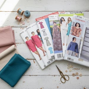 May include: A collection of sewing supplies including fabric, sewing patterns, spools of thread, buttons, and scissors. The fabric is in shades of pink, beige, and teal. The patterns feature images of dresses.