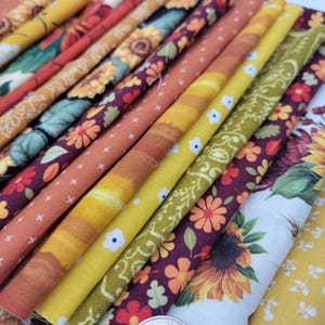 Op de afbeelding: Een verzameling stofresten met verschillende herfstpatronen, waaronder zonnebloemen, bladeren en paisley-patronen in tinten geel, oranje, bruin en bordeaux.